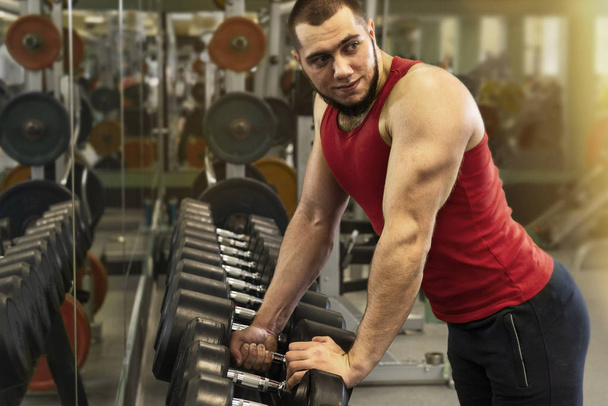Un tipo haciendo ejercicio en el gimnasio. Hombre fuerte toma pesas para el entrenamiento
. - Foto, imagen