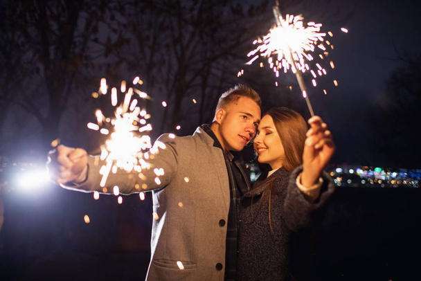 Selective focus of sparklers in hands of young couple enjoying holiday time outdoors - Valokuva, kuva