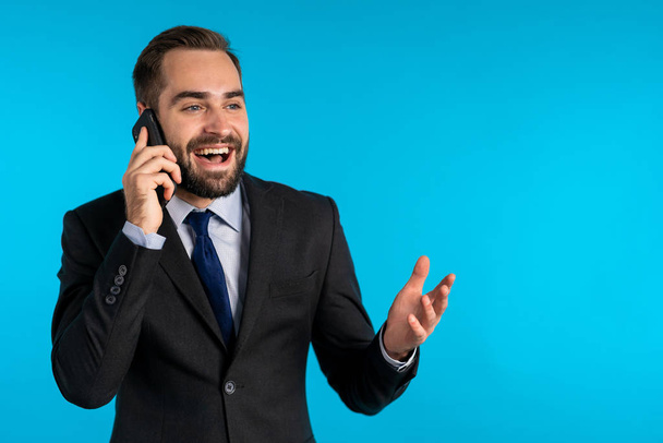 Businessman have conversation using mobile phone isolated on blue background. Business guy in formal suit gladly talks with colleague. Office employee, wage worker, weekdays concept. Copy space. - 写真・画像