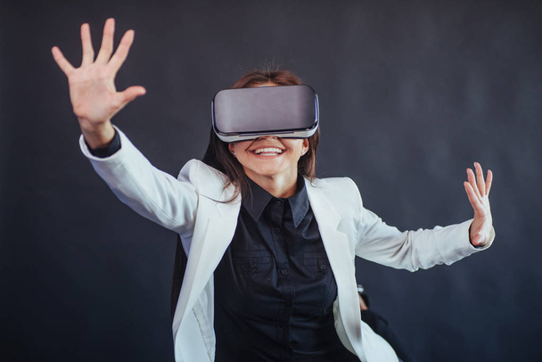 Happy woman on a black background in the studio gets the experience of using VR-glasses virtual reality headset - Φωτογραφία, εικόνα
