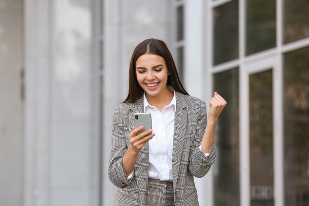 Happy young businesswoman with mobile phone outdoors - Photo, Image
