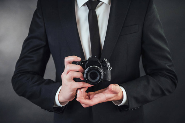 Business man holding black digital camera. In the studio on a dark background - Foto, Bild