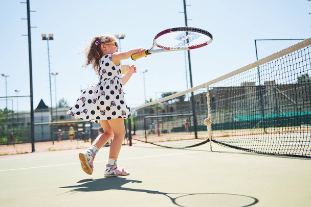 cute little girl playing tennis on the tennis court outside. - Foto, afbeelding