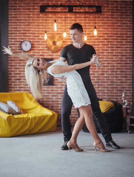 Young couple dancing latin music: Bachata, merengue, salsa. Two elegance pose on cafe with brick walls. - Photo, Image