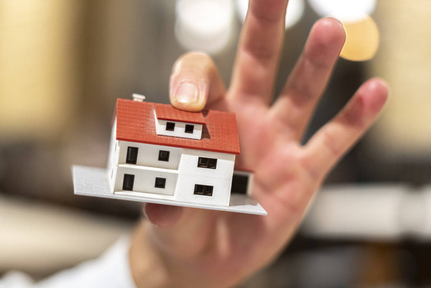 Immobilieninvestitionen. Wohnungsneubaukonzept. Männliche Hände und Finger halten ein Modell im Hausmaßstab - Foto, Bild