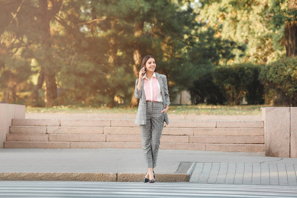 Beautiful young businesswoman crossing road outdoors - Фото, изображение