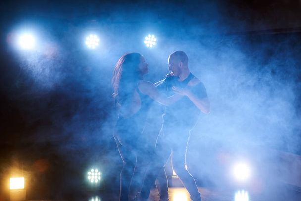 Skillful dancers performing in the dark room under the concert light and smoke. Sensual couple performing an artistic and emotional contemporary dance. - Foto, Bild