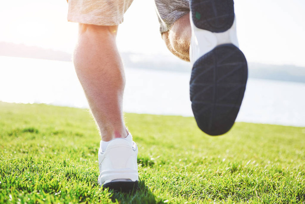 Outdoor cross-country running in summer sunshine concept for exercising, fitness and healthy lifestyle. Close up of feet of a man running in grass. - Photo, image