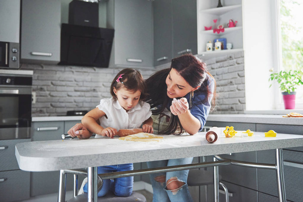 Happy family in the kitchen. Holiday food concept. Mother and daughter preparing the dough, bake cookies. Happy family in making cookies at home. Homemade food and little helper. - Foto, imagen