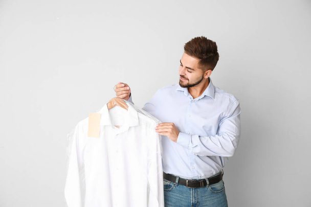 Male worker of modern dry-cleaner with clothes on light background - Zdjęcie, obraz