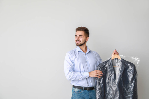 Male worker of modern dry-cleaner with clothes on light background - Foto, imagen
