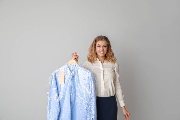 Female worker of modern dry-cleaner with clothes on light background - Photo, Image