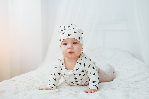 Newborn baby dressed in a white suit and black stars is a white soft bed in the studio. - Foto, afbeelding