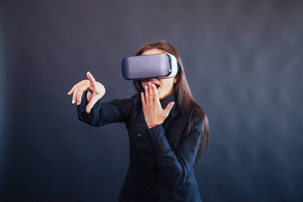 Happy woman on a black background in the studio gets the experience of using VR-glasses virtual reality headset - Foto, afbeelding