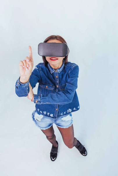 Fashion brunette beautiful woman posing in the studio, wearing jeans wear, using VR-glasses virtual reality headsets - Фото, зображення