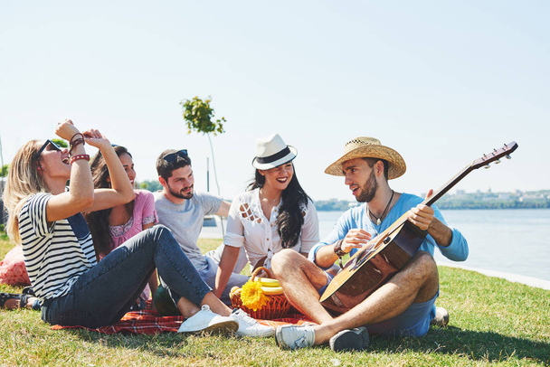 Happy young friends having picnic in the park.They are all happy,having fun,smiling and playing guitar. - 写真・画像