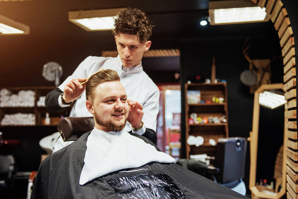The Barber man in the process of cutting the beard of client electric clippers in the barbershop - Фото, изображение