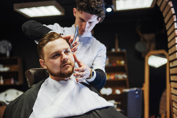 Man hairdresser doing haircut beard adult men in the men's hair salon. - Fotografie, Obrázek
