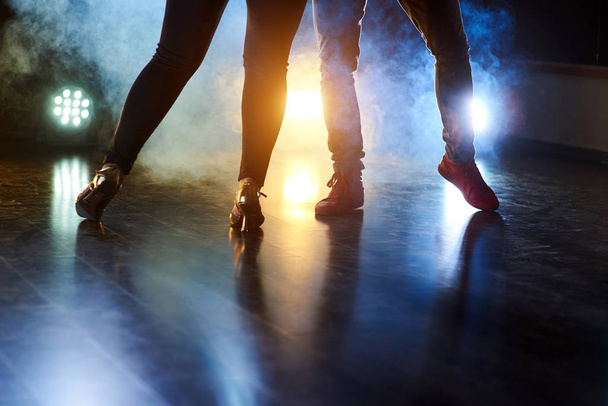 Умілі танцюристи виступають у темній кімнаті під концертним світлом і димом. Красива жінка і чоловічі ноги в активному танці
. - Фото, зображення