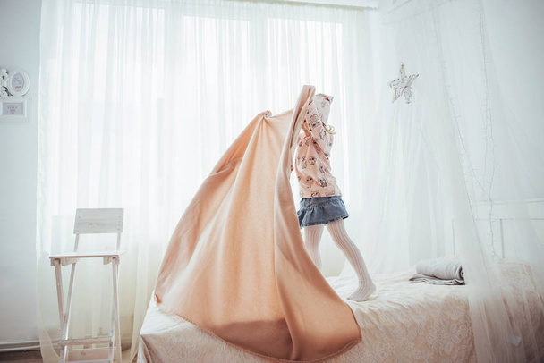 The little girl wants to wrap in a blanket in the bedroom light. - Foto, Imagen