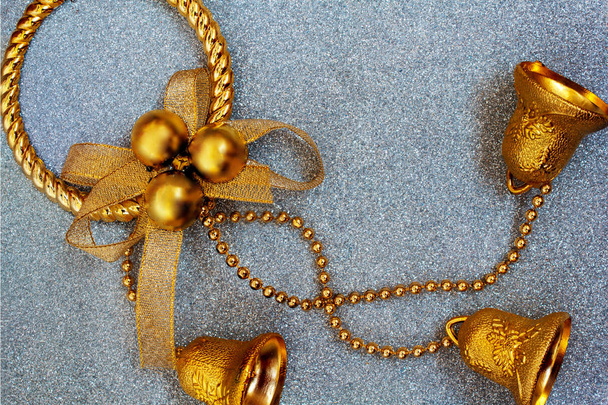 Brinquedo de Natal dourado na forma de uma grinalda com três sinos em um fundo de prata com brilhos multicores brilhantes. Foco seletivo suave, borrão, efeito bokeh. cartão de convite
 - Foto, Imagem