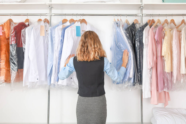 Young female worker near rack with clothes at dry-cleaner's - Foto, imagen