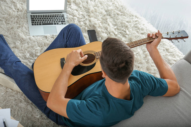 pohledný muž hraje doma na kytaru - Fotografie, Obrázek