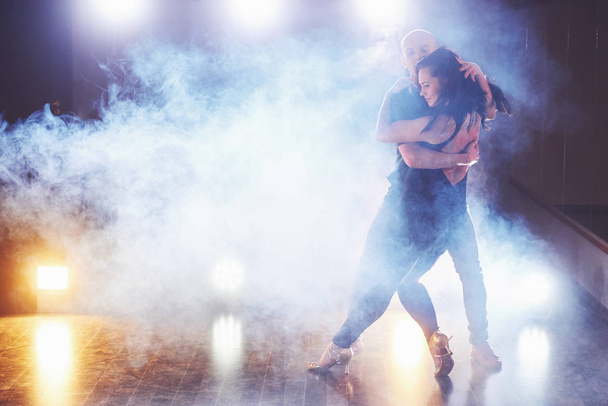 Skillful dancers performing in the dark room under the concert light and smoke. Sensual couple performing an artistic and emotional contemporary dance. - Foto, afbeelding