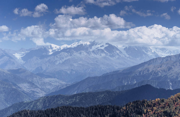 Fantásticas montañas cubiertas de nieve en las hermosas nubes de cúmulos. Principal cresta caucásica. Tipo Monte Ushba Meyer, Georgia
. - Foto, imagen