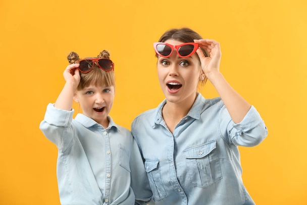 Portrait of surprised mother and daughter with sunglasses on color background - Foto, Imagem