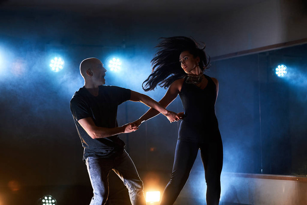 Skillful dancers performing in the dark room under the concert light and smoke. Sensual couple performing an artistic and emotional contemporary dance. - Foto, imagen