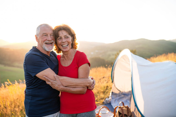 Senior tourist couple standing in nature at sunset, resting. - 写真・画像