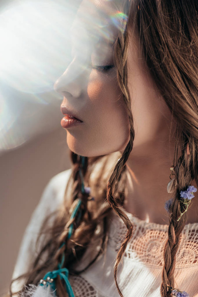 tender girl with closed eyes and braids in hairstyle posing in white boho dress on grey with lens flares  - Photo, Image