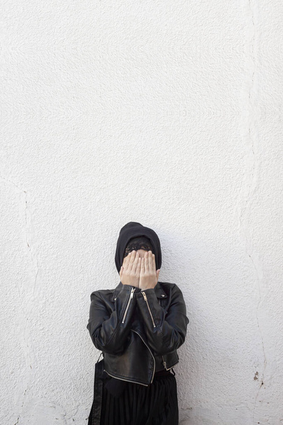 ヤシの木で顔を覆う若いイスラム教徒の少女。家庭内暴力や虐待の被害者。アラビア人の女性が顔を手で隠して恥じている - 写真・画像