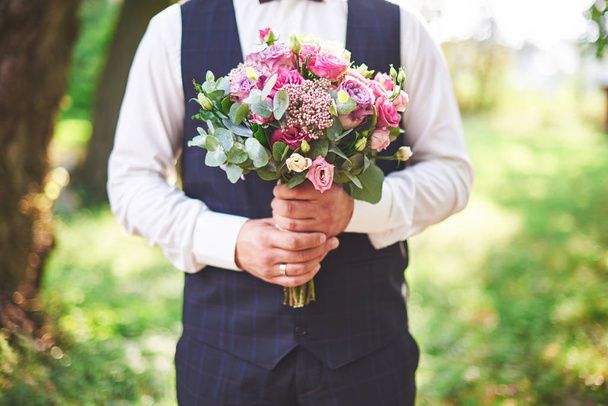 Stylish groom holding a tender pink wedding bouquet. - Фото, изображение