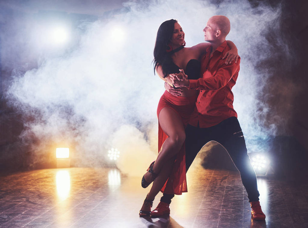 Skillful dancers performing in the dark room under the concert light and smoke. Sensual couple performing an artistic and emotional contemporary dance. - Photo, image
