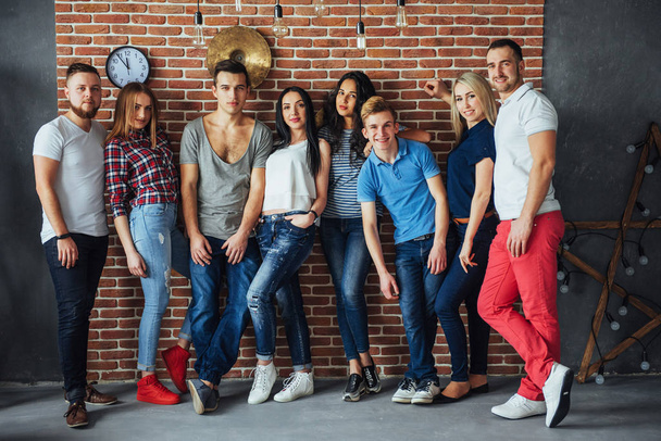 Group portrait of multi-ethnic boys and girls with colorful fashionable clothes holding friend and posing on a brick wall, Urban style people having fun, Concepts about youth and togetherness lifestyle. - Фото, изображение
