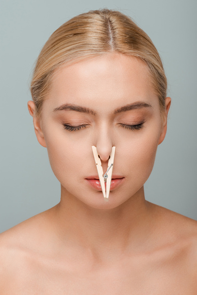 naked young woman with wooden pin on nose and closed eyes isolated on grey  - Foto, imagen