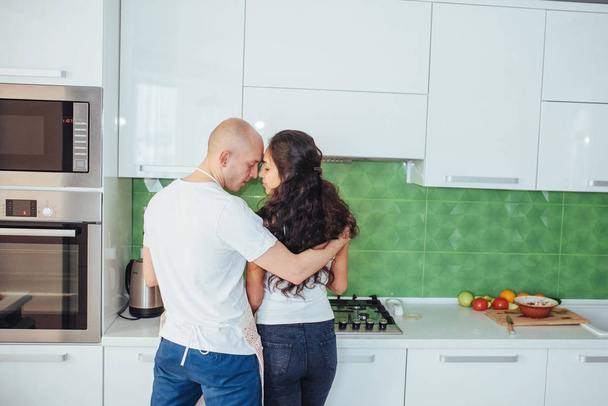 Beautiful young couple photographed smiling at the camera while cooking in the kitchen at home - Fotografie, Obrázek