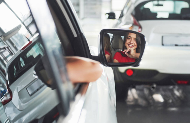 woman in car indoor keeps wheel turning around smiling looking at passengers in back seat idea taxi driver against sunset rays Light shine sky Concept of exam Vehicle - second home the girl. - Foto, afbeelding