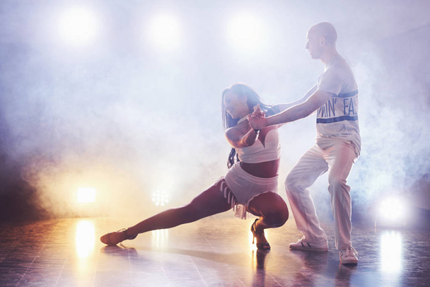 Skillful dancers performing in the dark room under the concert light and smoke. Sensual couple performing an artistic and emotional contemporary dance. - Foto, imagen