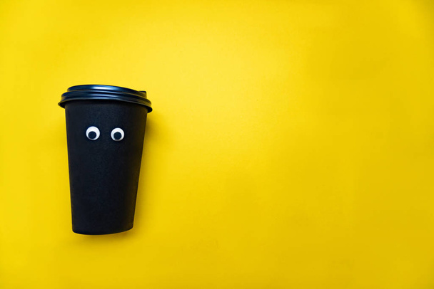 Coffee cup with googly eyes on yellow background - Zdjęcie, obraz