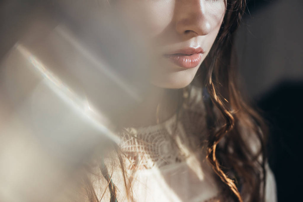 cropped view of boho girl with braids in hairstyle posing in white dress on grey with lens flares  - Фото, изображение
