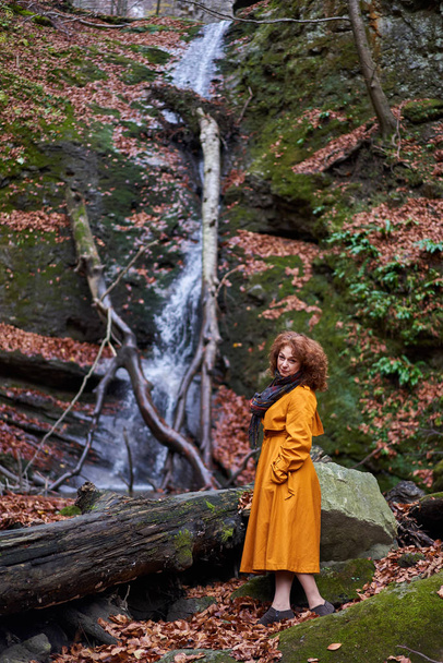 Portrait of a mature woman in yellow coat by a waterfall - Photo, image
