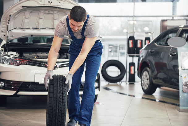 Mechanic holding a tire tire at the repair garage. replacement of winter and summer tires. - Fotoğraf, Görsel