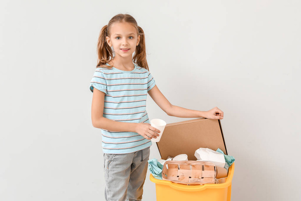 Little girl and container with trash on light background. Concept of recycling - Foto, Imagen