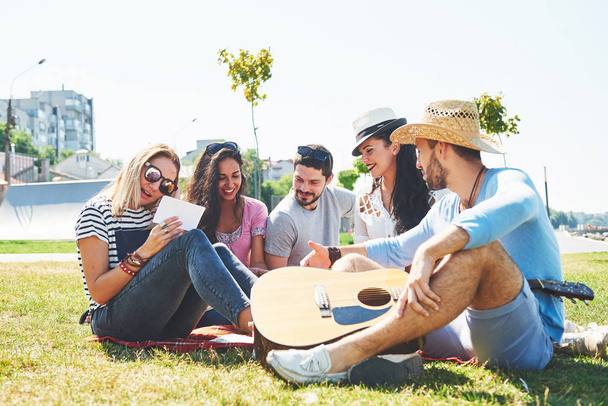 Happy young friends having picnic in the park.They are all happy,having fun,smiling and playing guitar. - Foto, imagen