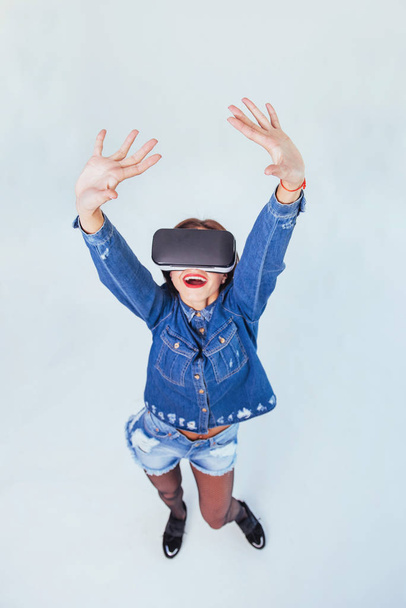 Fashion brunette beautiful woman posing in the studio, wearing jeans wear, using VR-glasses virtual reality headsets - Φωτογραφία, εικόνα