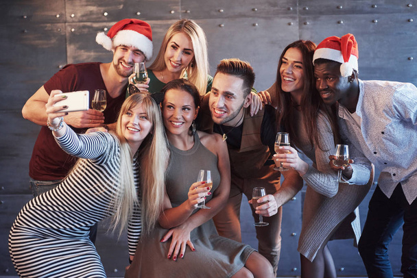 Group beautiful young people doing selfie in the new year party, best friends girls and boys together having fun, posing emotional lifestyle people. Hats santas and champagne glasses in their hands. - Zdjęcie, obraz