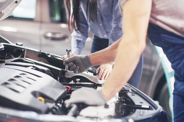 Een man monteur en vrouw klant kijken op de motorkap van de auto en bespreken van reparaties. - Foto, afbeelding